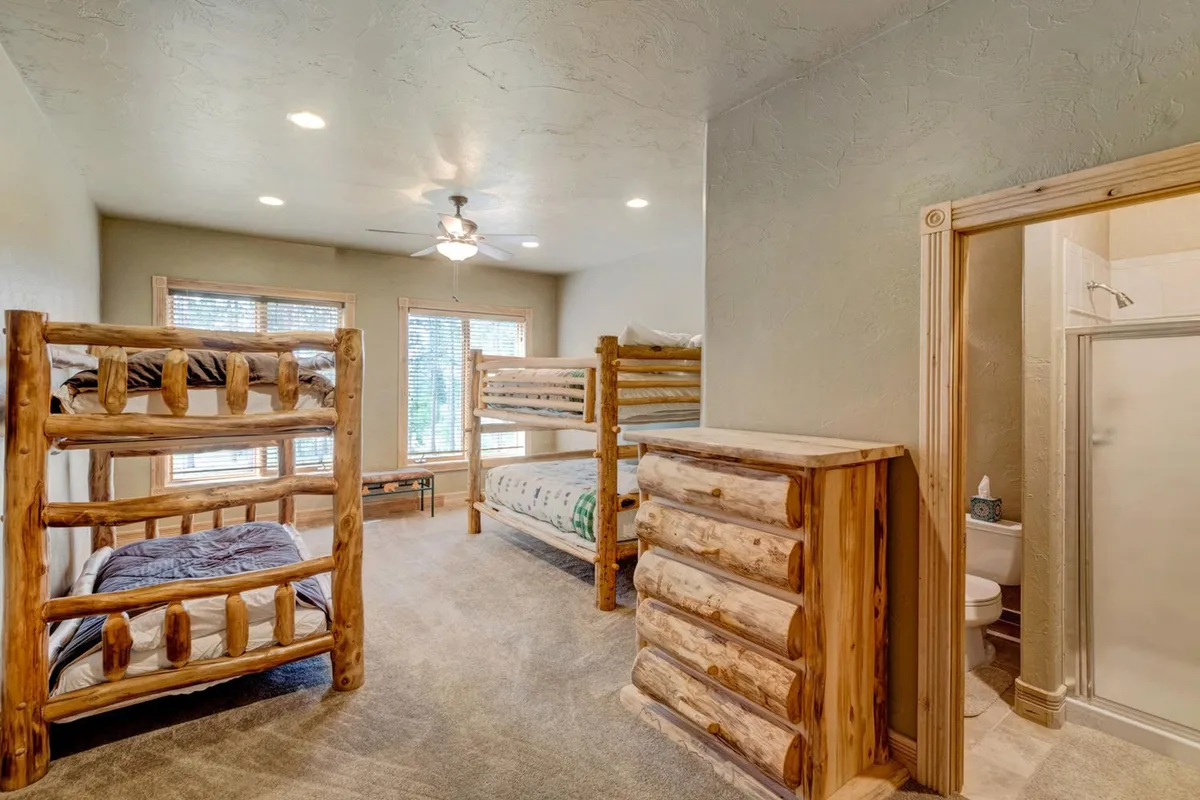 A custom-designed bunk room featuring multiple wooden bunk beds, a sturdy dresser, and windows letting in natural light. The space is clearly designed for children or groups, with a fun, family-friendly vibe.