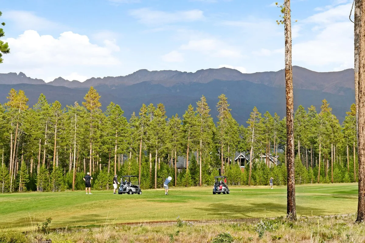 A vibrant scene with golfers on the course, golf carts, and the backdrop of distant mountains and tall pine trees. The active nature of the image emphasizes the leisure and social aspects of golfing at Pole Creek Golf Course.