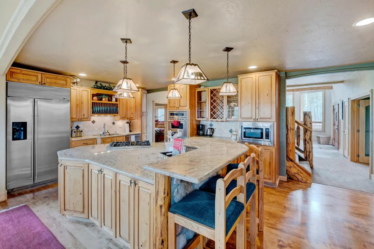 A close-up of the kitchen island area, highlighting stylish pendant lighting, granite countertops, wooden cabinetry, and stainless steel appliances. The image captures both the workspace for the chef and the inviting environment for guests to mingle.