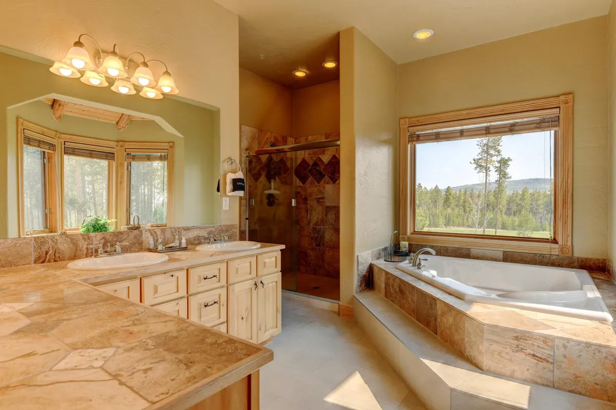 A spa-inspired bathroom with a large soaking tub, double sink vanity, glass-enclosed shower, and a window offering scenic outdoor views. The calming palette and luxury fixtures evoke a 5-star experience.
