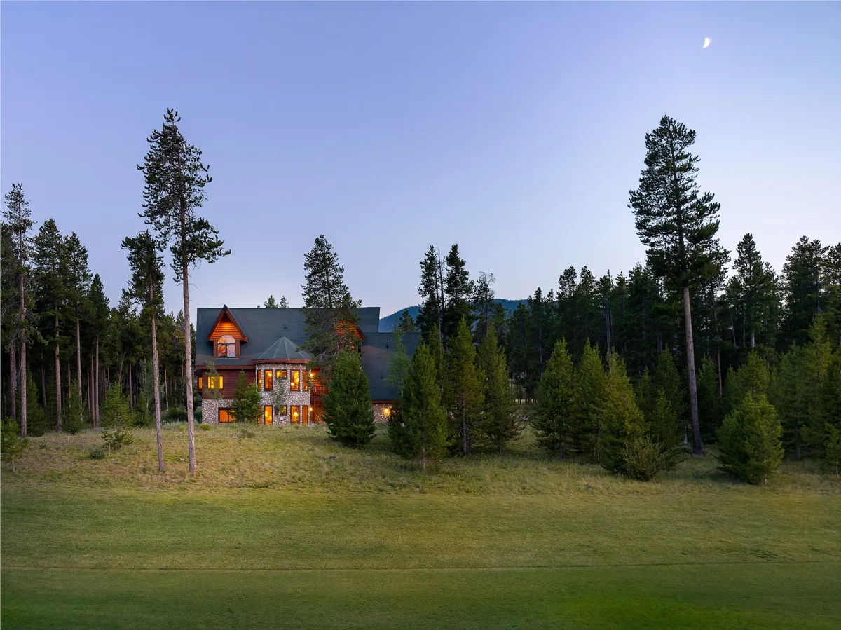The house glows warmly amid tall pine trees and distant mountain views. The outdoor setting evokes opportunities for stargazing, nature walks, and family gatherings, all in a tranquil mountain environment.