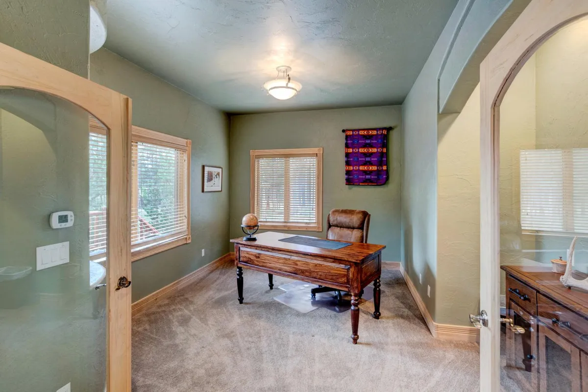 A serene home office setup with a wooden desk, ergonomic chair, tasteful wall art, and a window providing natural light through adjustable blinds. The atmosphere is quiet and conducive to focused work or moments of inspiration.