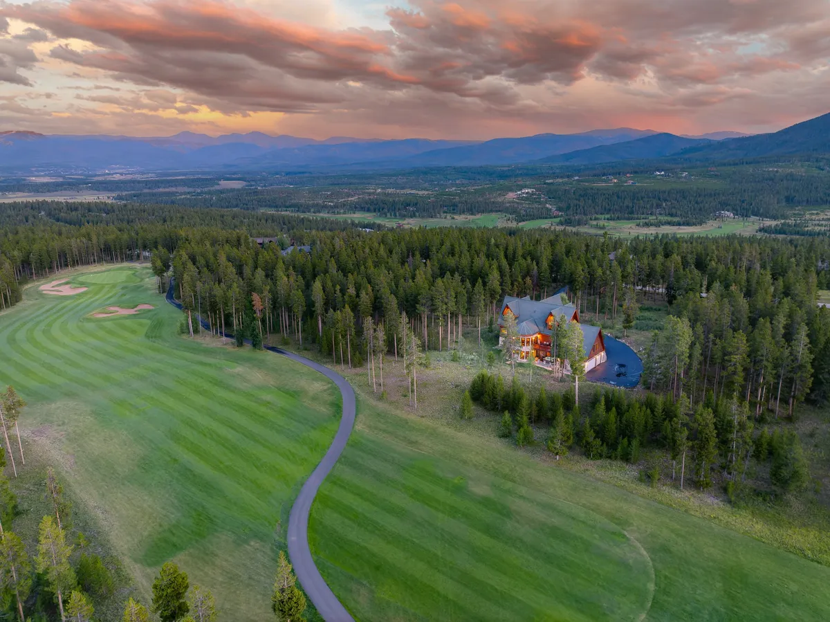 An exterior shot featuring the luxurious Three Peaks Chalet overlooking the lush fairways of the Pole Creek Golf Course, framed by majestic mountains and trees at sunset. The spacious patio hints at inviting outdoor gathering spaces and the seamless connection between the chalet and the surrounding recreation opportunities.